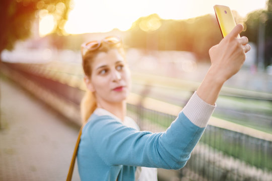 Woman taking selfie in park at sunset