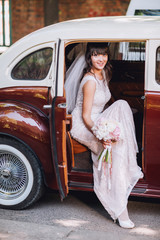 Gorgeous stylish brunette bride posing in retro brown and white limousine car in white dress. Woman...