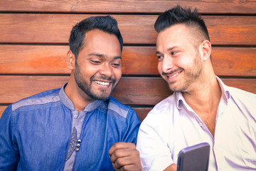 Multiracial young business men watching mobile phone screen and smiling - Indian man with caucasian friend having fun with smartphone - Concept of multicultural friendship 