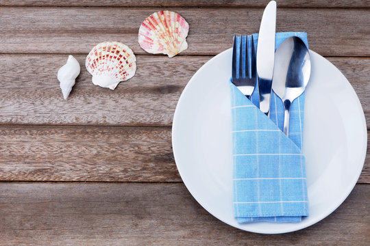 Top view of an empty white plate with cutlery on a wooden table.