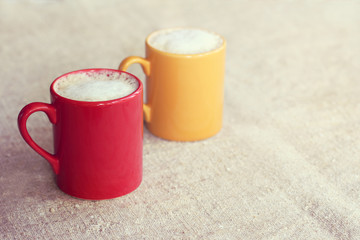 coffee for a couple with mood/ pair of colored mugs with frothy cappuccino stand on a desk 