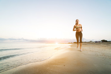 Cute fit girl running on beach at sunrise