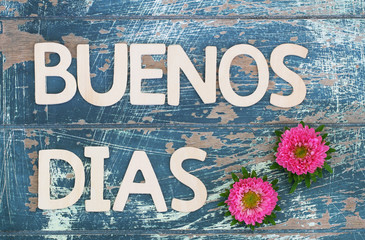 Buenos dias (good morning in Spanish) written with wooden letters and pink daisies
