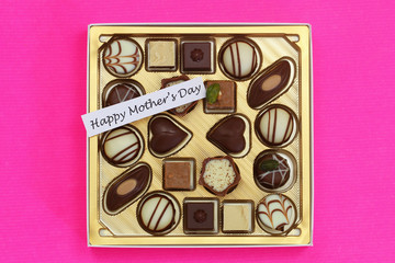Happy Mother's day card with box of assorted chocolates and pralines on pink surface
