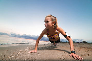 Cute fit girl doing push ups on beach at sunrise