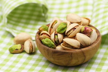 Pistachios in small wooden bowl on green and white checkered cloth
