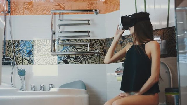 Girl sit on toilet. Looking in virtual reality glasses. Bathroom. Virtual world. Gadget