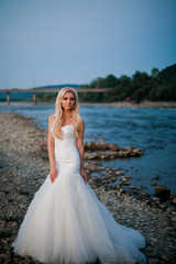 Fototapeta na wymiar Wonderful bride in amazing white dress on mountain river's coast