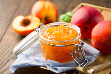 Jar of homemade peach jam with fresh fruits on rustic wooden table, selective focus