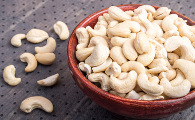 Raw cashew nuts in a brown bowl on fabric background