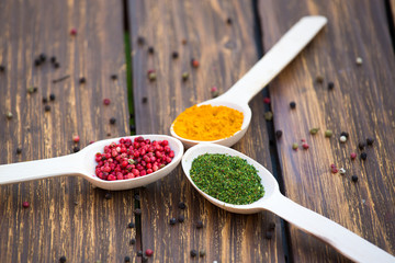 Three wooden spoons with colorful spices on wooden background