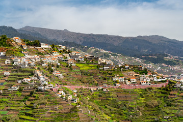 Fototapeta na wymiar Aerial view down valley in Portuguese Madeira Island in Atlantic ocean. High angle view down hillside into green valley with houses and roads in Madeira Portugal, image for travel business concept