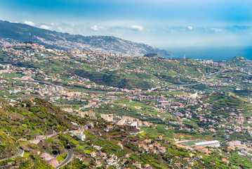 Aerial view down valley in Portuguese Madeira Island in Atlantic Ocean. 
High angle view down hillside into green valley with houses and roads in Madeira Portugal, image for travel business concept