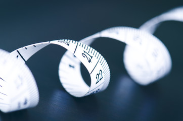 White measuring tape on a dark background. Rolled tape with numbers