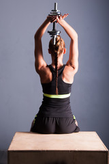 Athletic woman doing a fitness workout with Barbel weights for her back and arm muscles sit on the box