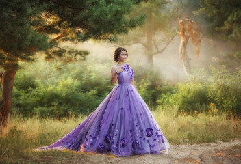 Naklejka premium Beautiful, young, brunette in a luxurious, purple, long dress. Fairy Photo. Creative toning. Queen walking in the fairy forest.