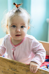 Fototapeta premium Close-up portrait of cute little baby girl with brunette hair in striped long sleeved bodysuit staying in rustic baby cot and looking at camera with thoughtful and curious beautiful eyes