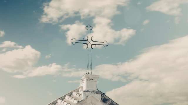 An old stone church over a cloudy mojo sky. Timelapse. Detail of the iron cross on the top.

