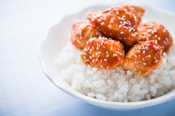 Spicy sweet and sour chicken with sesame and rice on blue wooden background. Oriental food.