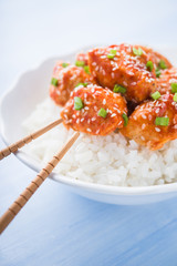 Spicy sweet and sour chicken with sesame and rice close up on blue background. Oriental food.
