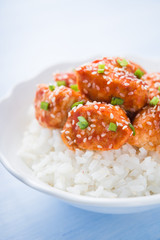 Spicy sweet and sour chicken with sesame and rice on blue wooden background close up. Oriental food.