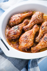 Baked spicy chicken legs with sesame on blue wooden background close up.