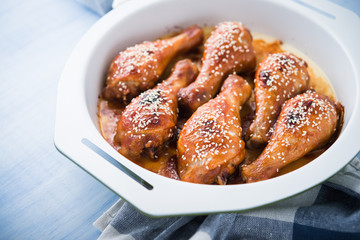 Baked spicy chicken legs with sesame on blue wooden background close up.
