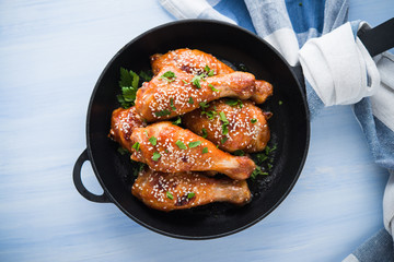 Baked spicy chicken legs with sesame and parsley in cast iron frying pan on blue wooden background top view. Asian food.