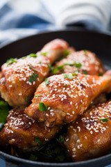Baked spicy chicken legs with sesame and parsley in cast iron frying pan on blue wooden background close up.