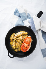 Dry basil parmesan fries and tomato chicken oven baked in cast-iron pan top view on white background.