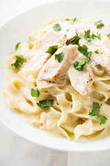 Pasta fettuccine alfredo with chicken, parmesan and parsley on white background close up. Italian cuisine.