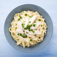 Pasta fettuccine alfredo with chicken, parmesan and parsley on blue wood background top view. Italian cuisine.