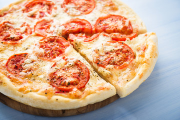 Sliced pizza with tomato, cheese and dry basil on blue wooden background close up. Italian cuisine.