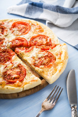Sliced pizza with tomato, cheese and dry basil on blue wooden background close up. Italian cuisine.