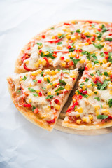 Sliced pizza with mozzarella cheese, chicken, sweet corn, sweet pepper and parsley on white background close up. Italian cuisine.