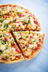 Colorful sliced pizza with mozzarella cheese, chicken, sweet corn, sweet pepper and parsley close up. Italian cuisine.