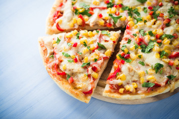 Colorful sliced pizza with mozzarella cheese, chicken, sweet corn, sweet pepper and parsley close up. Italian cuisine.