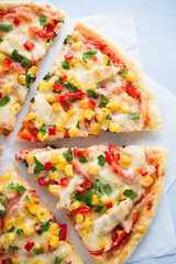 Colorful sliced pizza with mozzarella cheese, chicken, sweet corn, sweet pepper and parsley close up top view. Italian cuisine.