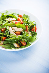 Fresh salad with chicken, tomato and greens (spinach, arugula) on blue wooden background close up. Healthy food.