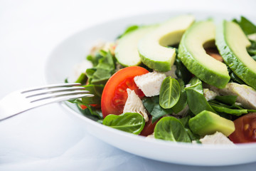 Fresh salad with chicken, tomatoes, spinach and avocado on white background close up. Healthy food.