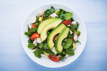 Fresh salad with chicken, tomatoes, spinach and avocado on blue wooden background top view. Healthy food.