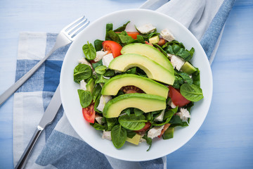 Fresh salad with chicken, tomatoes, spinach and avocado on blue wooden background top view. Healthy food.