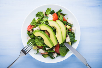 Fresh salad with chicken, tomatoes, spinach and avocado on blue wooden background top view. Healthy food.
