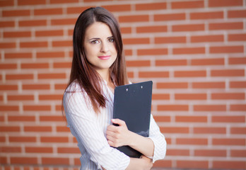 Smiling young elegant businesswoman with clipboard standing in a