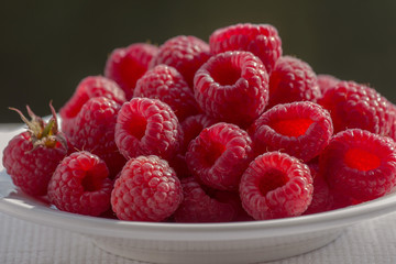 Raspberry in white bowl on the windowsill. Pyramid of raspberries. Delicious berries. Plate on a white napkin. Closeup. Natural light.