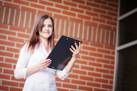 Smiling young elegant businesswoman with clipboard standing in a