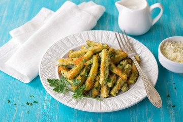 Baked zucchini in cheese batter with parsley, cheese and yogurt sauce on turquoise wooden table, selective focus