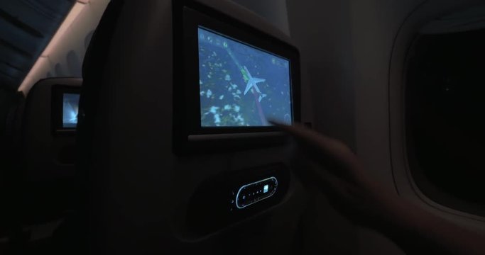 Woman using touchscreen seat monitor to look at flight path during night travel by plane