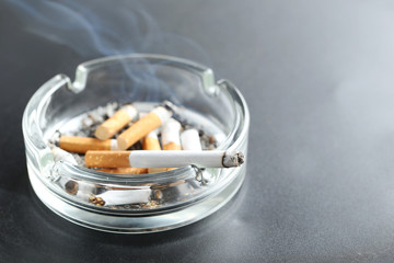 Cigarette butts with ash in ashtray on black background