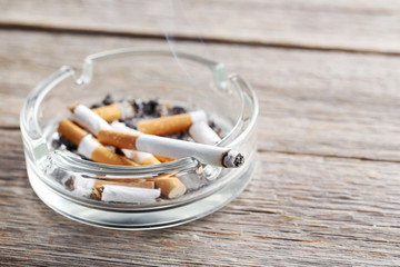 Cigarette butts with ash in ashtray on grey wooden table